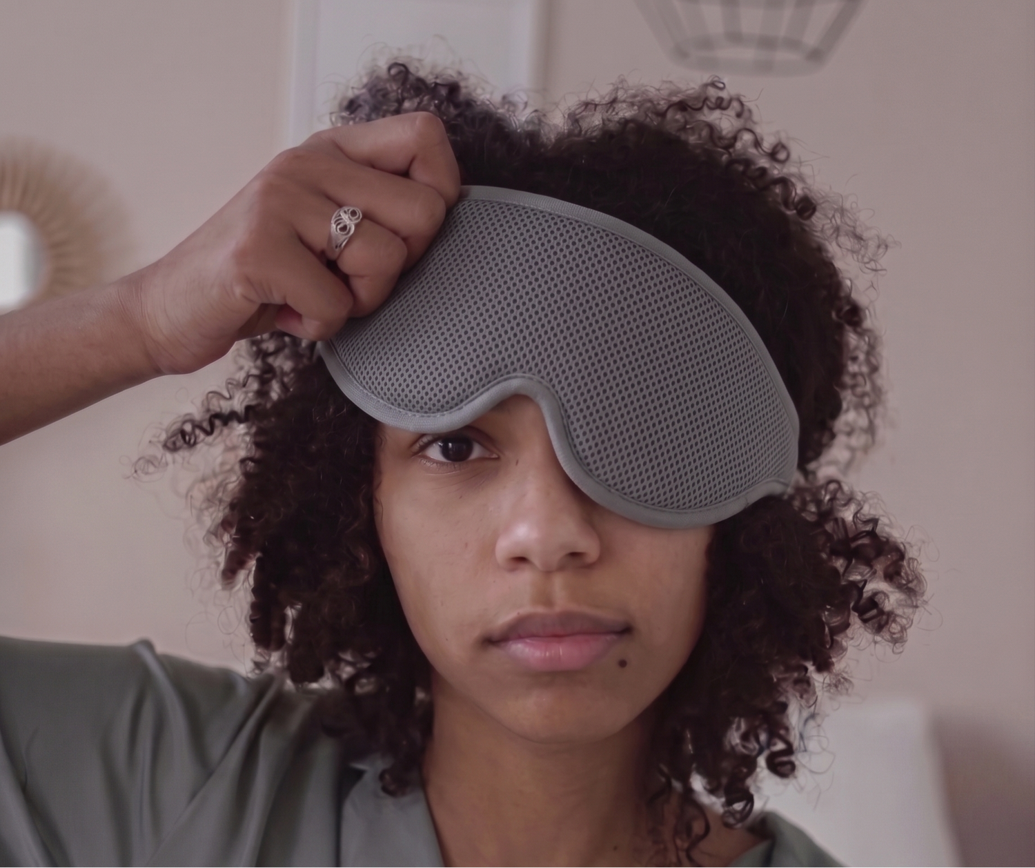Woman wearing a Rest'd gray sleep mask in a bedroom setting